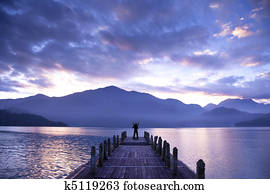 Man stand on a pier and watching the mountains and lake
