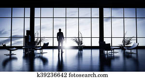 Business man standing in the office looking out of the window at sunset sky.