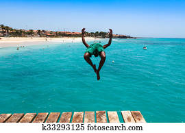 Teenage Cape verdean boy jumping on the turquoise  water of Santa Maria beach in Sal Cape Verde - Cabo Verde