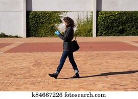 Caucasian woman wearing a protective mask and gloves walking in the streets, using her phone Caucasian woman wearing a protective mask and gloves walking in the streets, using her phone