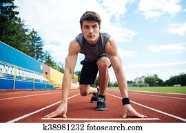 Young man in starting position for running on sports track