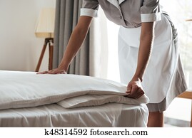 Cropped image of a chambermaid making bed in hotel room Cropped image of a chambermaid making bed in hotel room