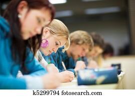 pretty female college student sitting an exam in a classroom full of students (shallow DOF; color toned image) pretty female college student sitting an exam in a classroom full of students (shallow DOF; color toned image)