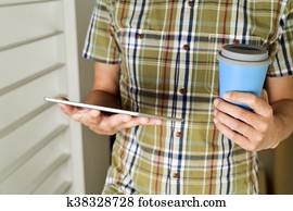 man with a cup of coffee or tea using a tablet