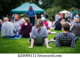 Friends sitting on the grass, enjoying an outdoors music, culture, community event, festival.
