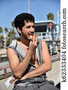 Ethnic young man eating pizza on the beach