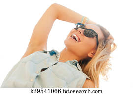 Enjoying sunshine. Low angle view of cheerful young woman holding hand in hair and smiling while standing outdoors