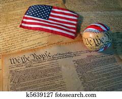 A copy of the Constitution of the United States accompanied by a flag and a baseball with the words of the Constitution on it.