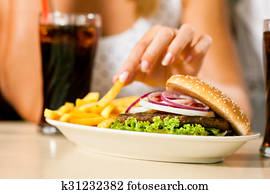 Two women eating hamburger and drinking soda