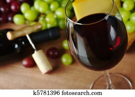 Red wine in wine glass with grapes, cheese a wine bottle and a corkscrew with cork in the background (Selective Focus, Focus on the front of the rim of the wine glass) Red wine in wine glass with grapes, cheese a wine bottle and a corkscrew with cork in the background (Selective Focus, Focus on the front of the rim of the wine glass)