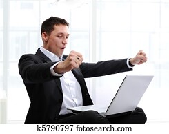 Happy executive raising fists in excitement, in front of laptop Happy executive raising fists in excitement, in front of laptop