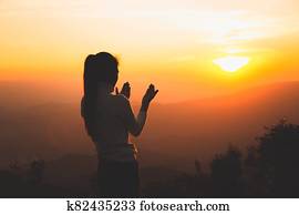 A women is praying to God on the mountain. Praying hands with faith in religion and belief in God on blessing background. Power of hope or love and devotion.