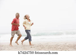 Senior Couple On Holiday Running Along Winter Beach