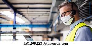 Technician or engineer with protective mask and laptop working in industrial factory.