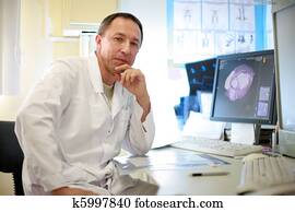A portrait of doctor sitting with CAT scan on the monitor and x-ray films on the table .