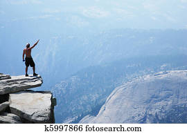 Man standing on top of a cliff with arm raised Man standing on top of a cliff with arm raised