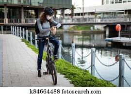Caucasian woman wearing a protective mask and a cycling helmet in the streets, checking her smar Caucasian woman wearing a protective mask and a cycling helmet in the streets, checking her smar
