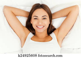 Beautiful day dreamer. Top view of beautiful young woman holding hands behind head while lying in bed and smiling
