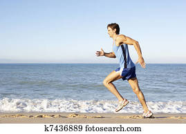 Young Man In Fitness Clothing Running Along Beach