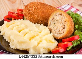 two fried breaded cutlet with mashed potatoes and lettuce on a black plate wooden background