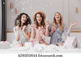 Portrait of beautiful excited women 20s wearing dresses celebrating bridal shower in posh apartment, with champagne and falling confetti Portrait of beautiful excited women 20s wearing dresses celebrating bridal shower in posh apartment, with champagne and falling confetti