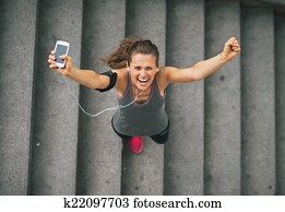 Portrait of happy fitness young woman with cell phone outdoors i