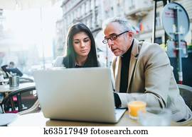 Man and woman business partners with laptop sitting in a cafe in city, talking.