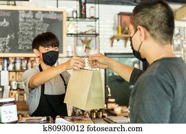 Social distance conceptual waiter giving takeaway bag to customer at cafe.