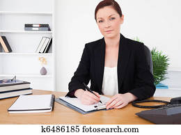 Attractive red-haired female in suit writing on a notepad 