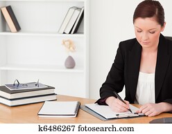 Attractive red-haired woman in suit writing on a notepad