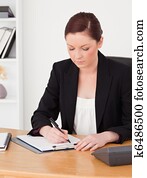 Beautiful red-haired woman in suit writing on a notepad