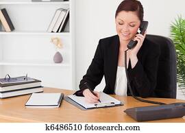 Beautiful red-haired woman in suit writing on a notepad and phone