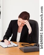 Depressed beautiful red-haired woman in suit writing on a notepad
