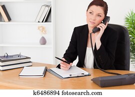 Good looking red-haired woman in suit writing on a notepad 