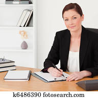 Good looking red-haired woman in suit writing on a notepad