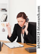 Infuriated beautiful red-haired woman in suit phoning