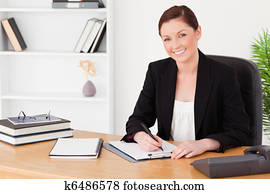 Pretty red-haired woman in suit writing on a notepad