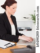 Young attractive red-haired woman in suit typing on her laptop