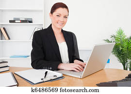 Young beautiful red-haired female in suit typing on her laptop