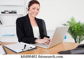 Young beautiful red-haired female in suit typing on her laptop 