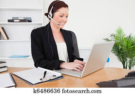 Young good looking red-haired female in suit typing on her laptop