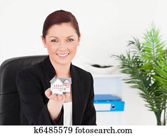 Young pretty red-haired woman in suit holding a miniature house