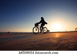 Biker silhouette riding along beach at sunset Biker silhouette riding along beach at sunset