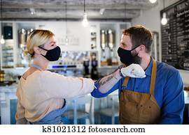 Coffee shop owners with face masks elbow bumping, open after lockdown quarantine.