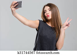 Woman making selfie photo on smartphone and showing peace sign