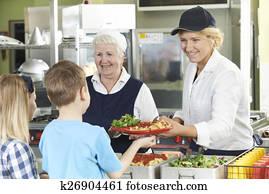 Pupils In School Cafeteria Being Served Lunch By Dinner Ladies