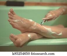 Female foots in the bathroom. The girl shaves her legs. Photo is out of focus. Female foots in the bathroom. The girl shaves her legs. Photo is out of focus.