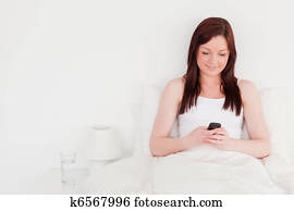 Attractive red-haired woman writing a text on her mobile 