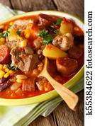 National cuisine of Cape Verde: Cachupa with meat, chorizo and vegetables close-up on a plate. vertical