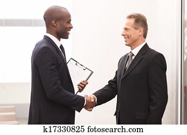 Business meeting. Two cheerful business men shaking hands and looking at each other Business meeting. Two cheerful business men shaking hands and looking at each other